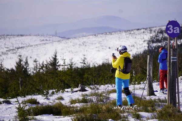 Szczyrk, Polônia 15.01.2020: uma mulher com roupas de esqui azuis e amarelas fotografa uma vista das montanhas em um dia ensolarado e claro no pico da montanha. recreação de inverno ativo — Fotografia de Stock