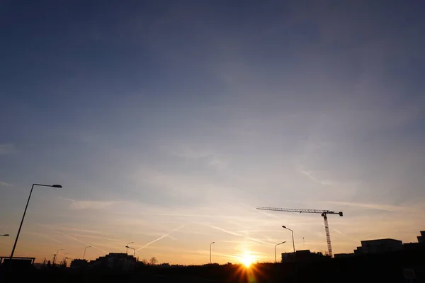 Niesamowite jasne miasto zachód słońca czyste błękitne niebo. Sylwetki masztów oświetleniowych i suwnic budowlanych. Romantyzm życia i wieczornych spacerów — Zdjęcie stockowe