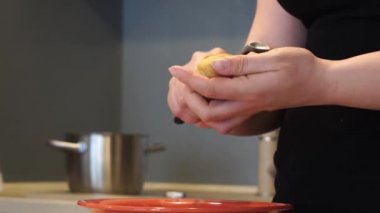 Bir kadın, arka planda bir bıçakla çiğ sarı patatesleri parçalara ayırıyor, ev yapımı yemekler pişiriyor..