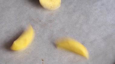 Yakın planda, bir kadın fırında pişirmek için tereyağlı, tuzlu ve baharatlı patatesleri fırın kağıdıyla kaplı bir kabın üzerine koyar. Ev yemeği, yemek.
