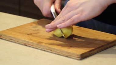 Bir kadın, arka planda bir bıçakla çiğ sarı patatesleri parçalara ayırıyor, ev yapımı yemekler pişiriyor..