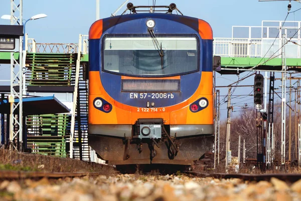 El tren eléctrico naranja y azul en la estación de tren. Pista, postes y soportes para líneas de transporte de corriente . — Foto de Stock