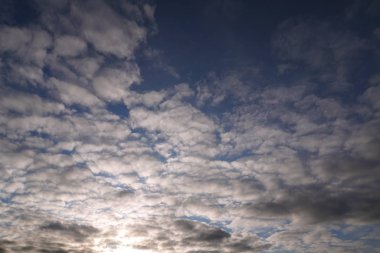 Mavi gökyüzünde beyaz, tüylü bulutlar ve güneş patlaması..