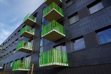Poland, Krakow 02.16.2020: Modern multi-storey residential building with black facade finish and bright green and yellow balconies in Europe. Townhouse in modern style