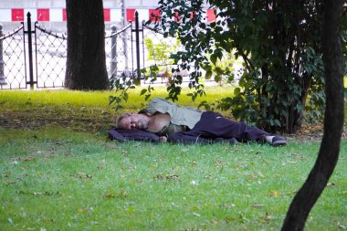Krakow, Poland - 07.27.2019: dirty homeless man sleeps on the lawn under a tree in the Park. bums in the center of the big city. beggars - the problem of tourist cities.