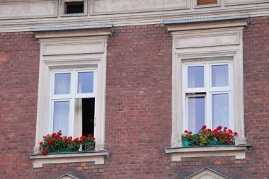Çiçeklerle süslenmiş eski evdeki iki pencere. Yamaçların yenilenmiş cephesi. Duvarlar kırmızı tuğladan.