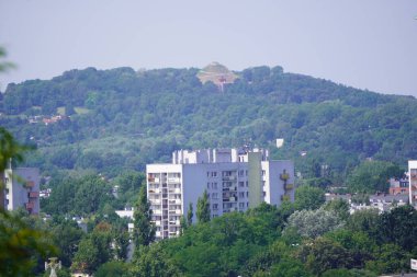 Tepelerdeki modern şehir manzarası, taş binalar. Uzakta farklı tarz evler var. Bir sürü yeşilliği, uzun ağaçları olan bir şehir.