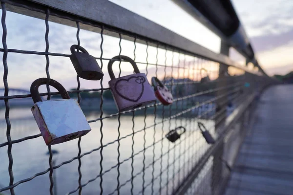 modern bridge in sunset light, colored sky and clouds, city sunset by the river, water. evening promenade, walk. locks on the bars on the wedding day, tradition