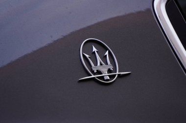 Maserati logo on the body of a gray car. Luxury Italian car. Trident, metal. clipart