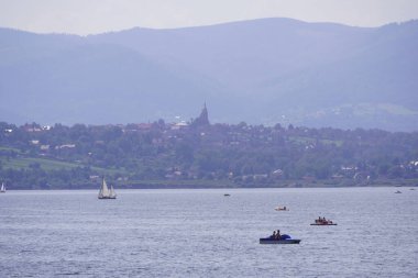 Beyaz yelkenli yat, dağların ve ormanların arka planına karşı gölde. Kamp manzarası, karavanlar, minibüs hayatı. Çadırda dinlenmek, ateşte yemek ve kamp banyosu.