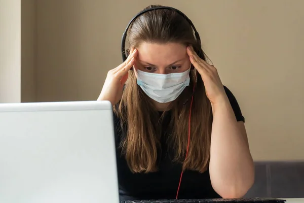 A girl in a medical mask works at home at the computer during the quarantine due to the coronavirus. Prevention of respiratory diseases. Remote work at home.