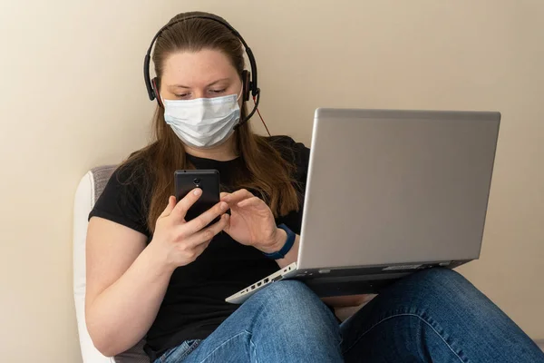 A girl in a medical mask works at home at the computer during the quarantine due to the coronavirus. Prevention of respiratory diseases. Remote work at home.