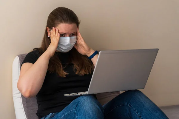 Girl in a medical mask works at home at the computer during quarantine due to the coronavirus. Prevention of respiratory diseases. Remote work at home. Quarantine, work from home. Problems