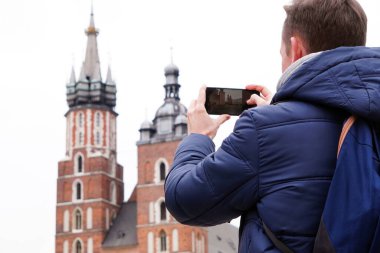 Bir erkek turist cep telefonuyla eski şehrin görüntülerini çekiyor. Mobil fotoğrafçılık. Turizm, Cazibe. Eski Avrupa şehri.