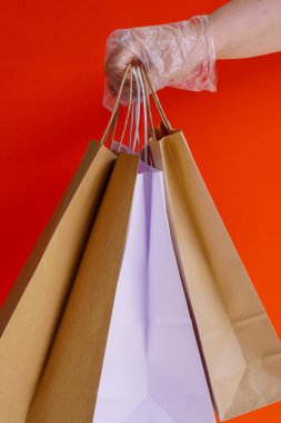 Plastik eldiven ya da plastik eldiven kırmızı arka planda kağıt eko-el işi poşetler tutar. Koronavirüs sırasındaki hediyeler. Virüs koruması, sosyal mesafeler. İnternetten karantina alışverişi. Çevre dostu gıda teslimatı