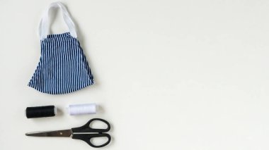 Koronavirüs, enfeksiyon ya da alerji sırasında tekrar kullanılabilir ve yıkanabilir pamuk maske dikmek. Beyaz arka planda iplik, makas ve mavi-beyaz çizgili maske. DIY, el yapımı ürün..