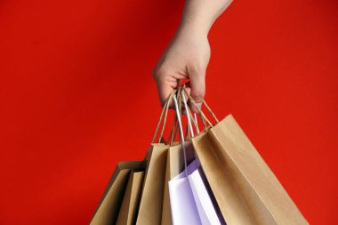Beyaz kağıt torbalarla el ve parlak kırmızı arka planda el işi. Bayram hediyesi olarak Noel alışverişi. Noel alışverişi. Ürünlerin çevre dostu paketlemede kurye teslimatı. Boşluğu kopyala