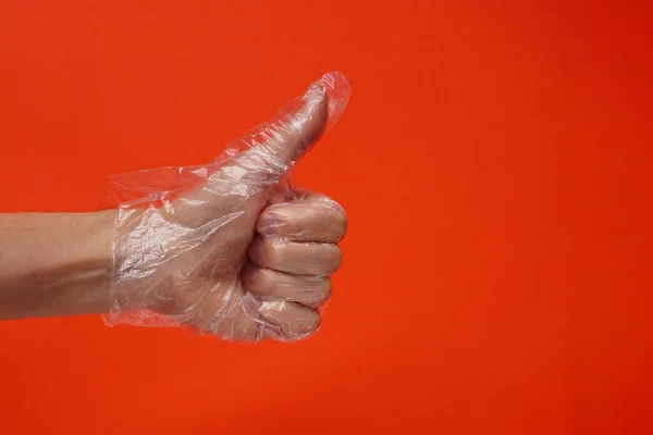Bir el plastik ya da plastik kaplı tek kullanımlık eldivenler kırmızı arka planda. Koronavirüs pandemiği sırasında virüslere ve bakterilere karşı korunma. İşareti, kopyalama alanını, tamam veya işaret kavramını parmakla.