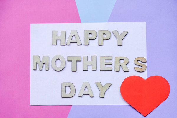 Happy mother day lettering in wooden letters on colored background. Pink and blue, red heart, blank for designers, space for text.