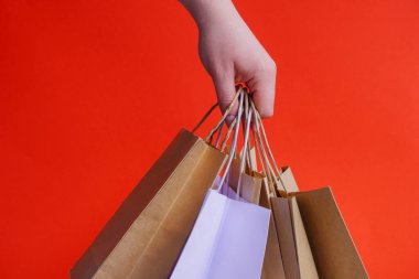 Beyaz kağıt torbalarla el ve parlak kırmızı arka planda el işi. Bayram hediyesi olarak Noel alışverişi. Noel alışverişi. Ürünlerin çevre dostu paketlemede kurye teslimatı. Boşluğu kopyala