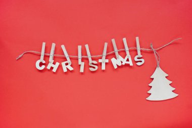 Noel düzlüğü, ahşap kelime Noel ve parlak kırmızı arka planda asılı duran bir Noel ağacı. Tatiller için doğal dekorasyon..