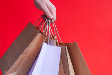 Beyaz kağıt torbalarla el ve parlak kırmızı arka planda el işi. Bayram hediyesi olarak Noel alışverişi. Noel alışverişi. Ürünlerin çevre dostu paketlemede kurye teslimatı. Boşluğu kopyala
