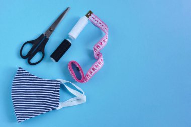 Koronavirüs, enfeksiyon ya da alerji sırasında tekrar kullanılabilir ve yıkanabilir pamuk maske dikmek. İplik, makas, mezura ve beyaz arka planda mavi-beyaz çizgili maske. DIY, el yapımı ürün.