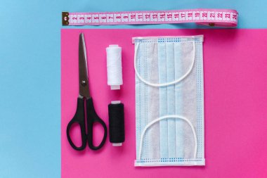 Koronavirüs, enfeksiyon ya da alerji sırasında tekrar kullanılabilir ve yıkanabilir pamuk maske dikmek. İplik, makas, mezura ve mavi ve pembe arka planda mavi-beyaz çizgili maske. DIY, el yapımı ürün.