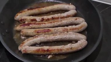 Sosisler kızartma tavasında yağda kızartılır. Karantina sırasında evde yemek pişirme süreci. Yağlı yiyecekler. Zaman Uygulaması