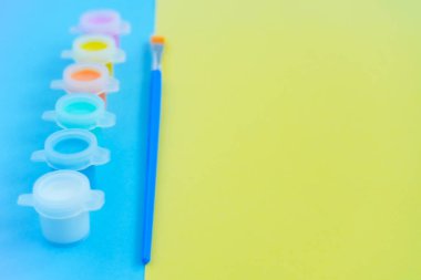 Renkli akrilik ya da suluboya boya kutuları ve mavi ve sarı arka planda fırçalar, çocuklarla yaratıcılığa ayarlı. DIY, el yapımı. Boşluğu kopyala, Flatley