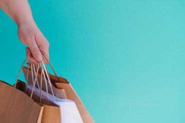 Beyaz kağıt torbalarla el ve açık yeşil ya da akuamarin arka planda el işi. Bayram hediyesi olarak Noel alışverişi. Noel alışverişi. Ürünlerin çevre dostu dağıtımı. Boşluğu kopyala