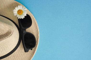 Hasır şapkalı, papatyalı ve güneş gözlüklü yaz düzeni. Seyahat ve eğlence kavramının en üst noktası. Denize uçuşlar, koronavirüs sırasında dinlenme. Flatlay on blue with copy-space. Moda detayları.