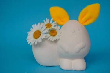 Beyaz tavşan ya da parlak sarı kulaklı tavşan ve mavi arka planda papatyalar. Yaban bahar çiçekli tavşan. Çocuklarla yaratıcılık.