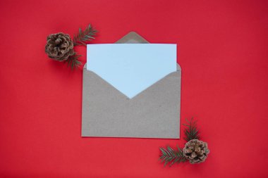 Noel çerçevesi düz, koniler ve Noel ağacı, içinde notlar için el işi zarfı ve beyaz kağıt olan parlak kırmızı zemin üzerine eko kağıt hediye kutusu. Tatiller için doğal dekorasyon.