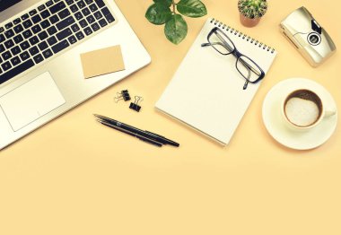 Yellow office table with laptop, green plants, pens, glasses, camera and cup of coffee. Top view with copy space, flat lay.