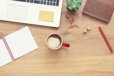 Wooden office desk table with notebook, laptop, glasses, plant, red cup of cappuccino and other office supplies. Top view with copy space, flat lay.
