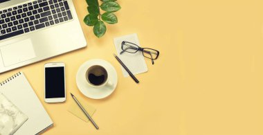 Flat lay, top view, copy space. Office yellow table desk. Workspace with plant, pen, pencil, notebook, computer, glasses, keyboard and cappuccino on beige background