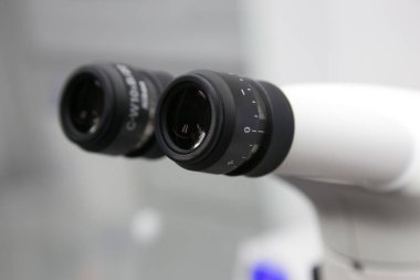 Metalik göz merceğinin yakın fotoğrafını beyaz optik mikroskop ameliyathanede steril tutuyor. İlaç araştırma konsepti için tıbbi biyoloji aygıtı teknolojisi ekipmanı.