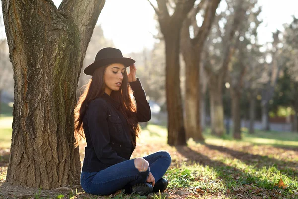 Thoughtful woman sitting alone outdoors wearing hat — Stock Photo, Image