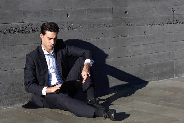 Businessman using a laptop computer sitting in the street — Stock Photo, Image