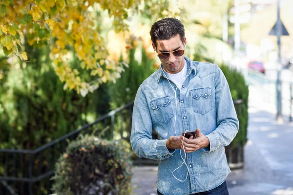 Joven en el fondo urbano escuchando música con auriculares — Foto de Stock