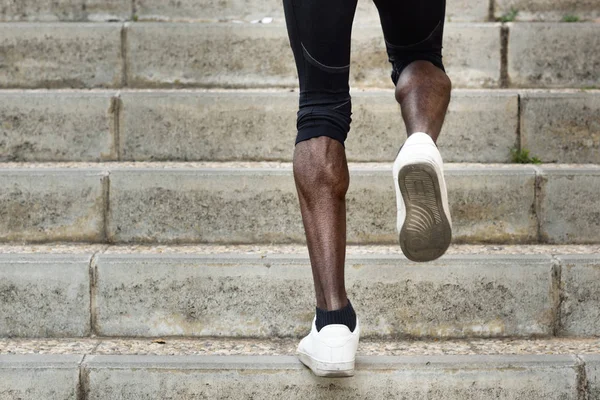 Sportliche Beine eines schwarzen Mannes, der auf Treppenstufen läuft. — Stockfoto
