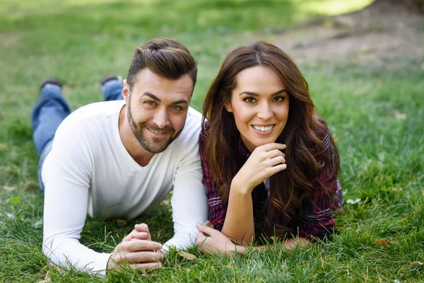 Beautiful young couple laying on grass in an urban park. — Stock Photo, Image
