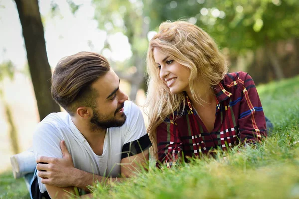 Belo jovem casal que coloca na grama em um parque urbano . — Fotografia de Stock