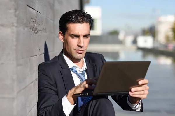 Uomo d'affari che utilizza un computer portatile seduto in strada — Foto Stock