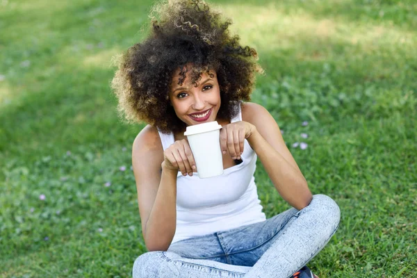 Donna con acconciatura afro bere caffè nel parco — Foto Stock