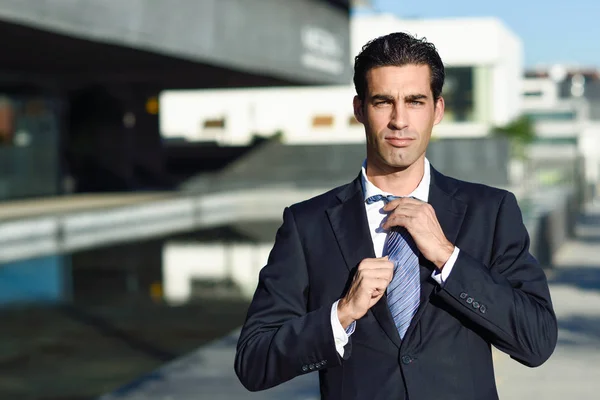 Young handsome businessman adjusting a tie in urban background — Stock Photo, Image