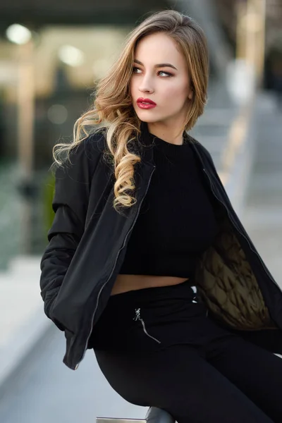 Beautiful young girl wearing black jacket sitting in the street. — Stock Photo, Image