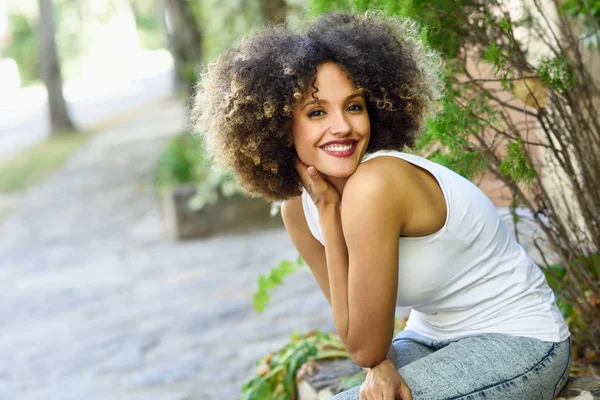 Jonge zwarte vrouw met afro kapsel glimlachend in stadspark — Stockfoto