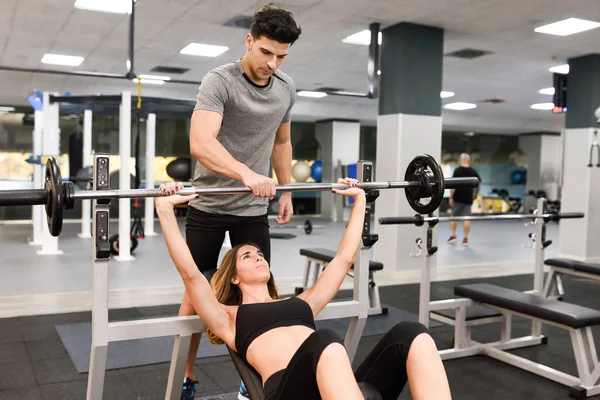 Προσωπικό γυμναστή βοηθά μια νεαρή γυναίκα άρση βαρών — Φωτογραφία Αρχείου